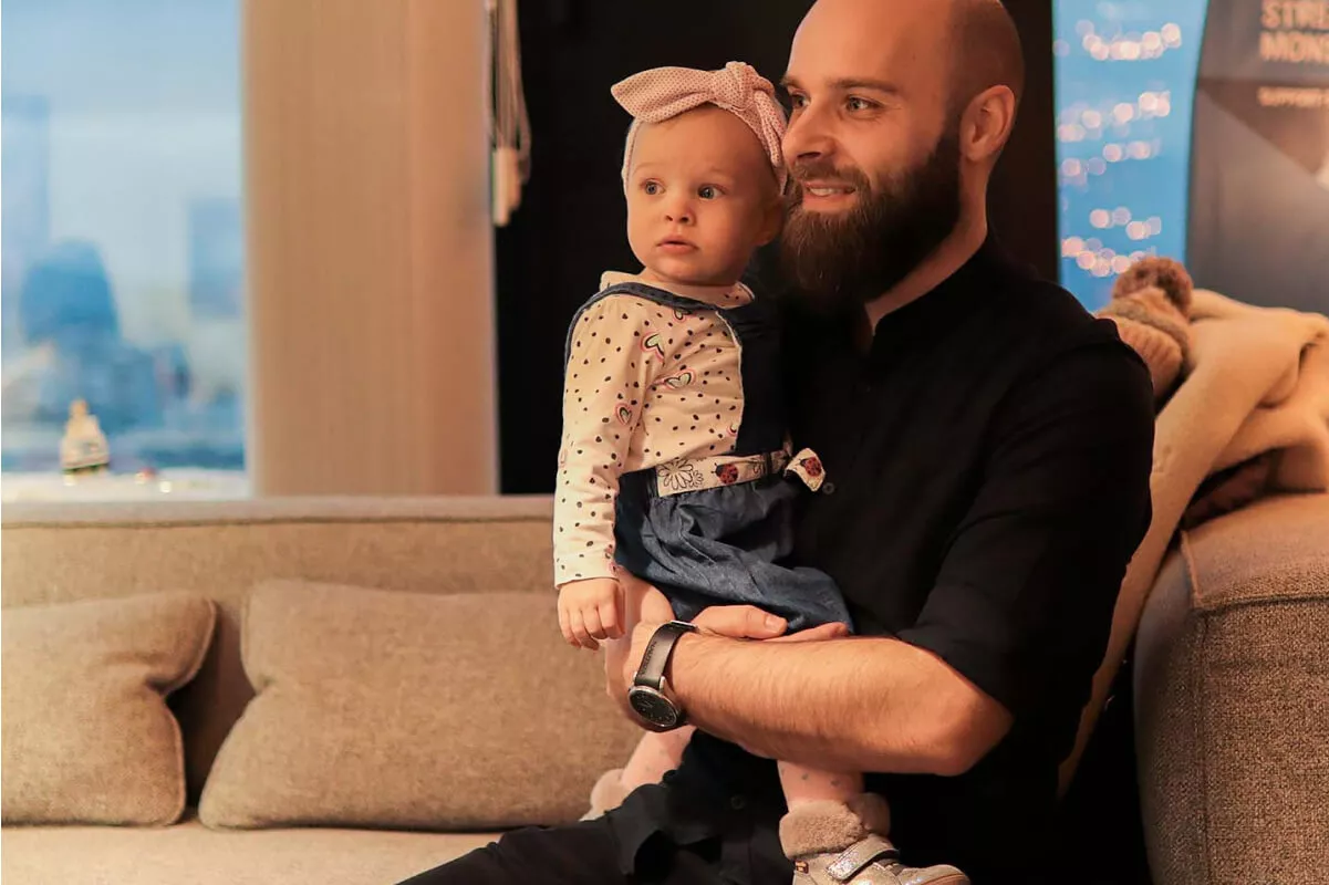 Man with a beard holds a baby wearing a bow headband.