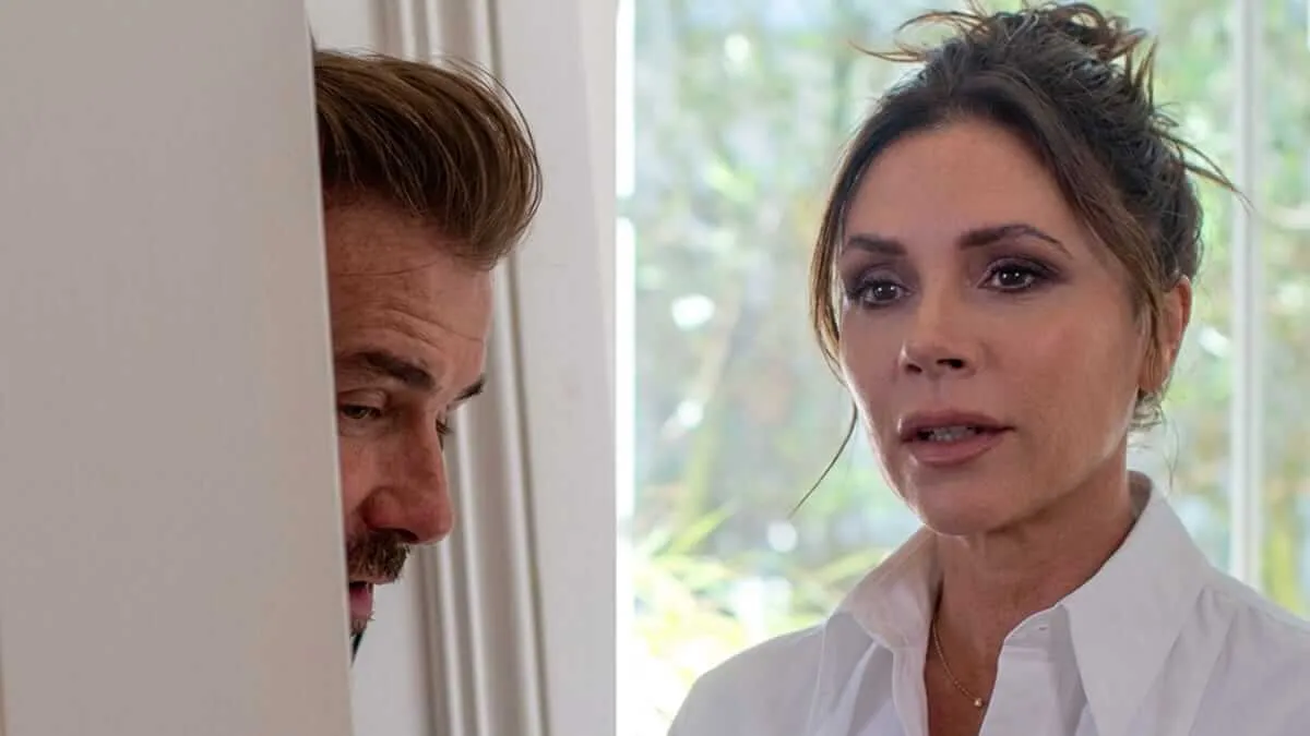 David Beckham peeking around a door on the left; Victoria Beckham speaking candidly on camera on the right, in a scene from their Netflix documentary where David challenges her to be honest about her working-class upbringing.